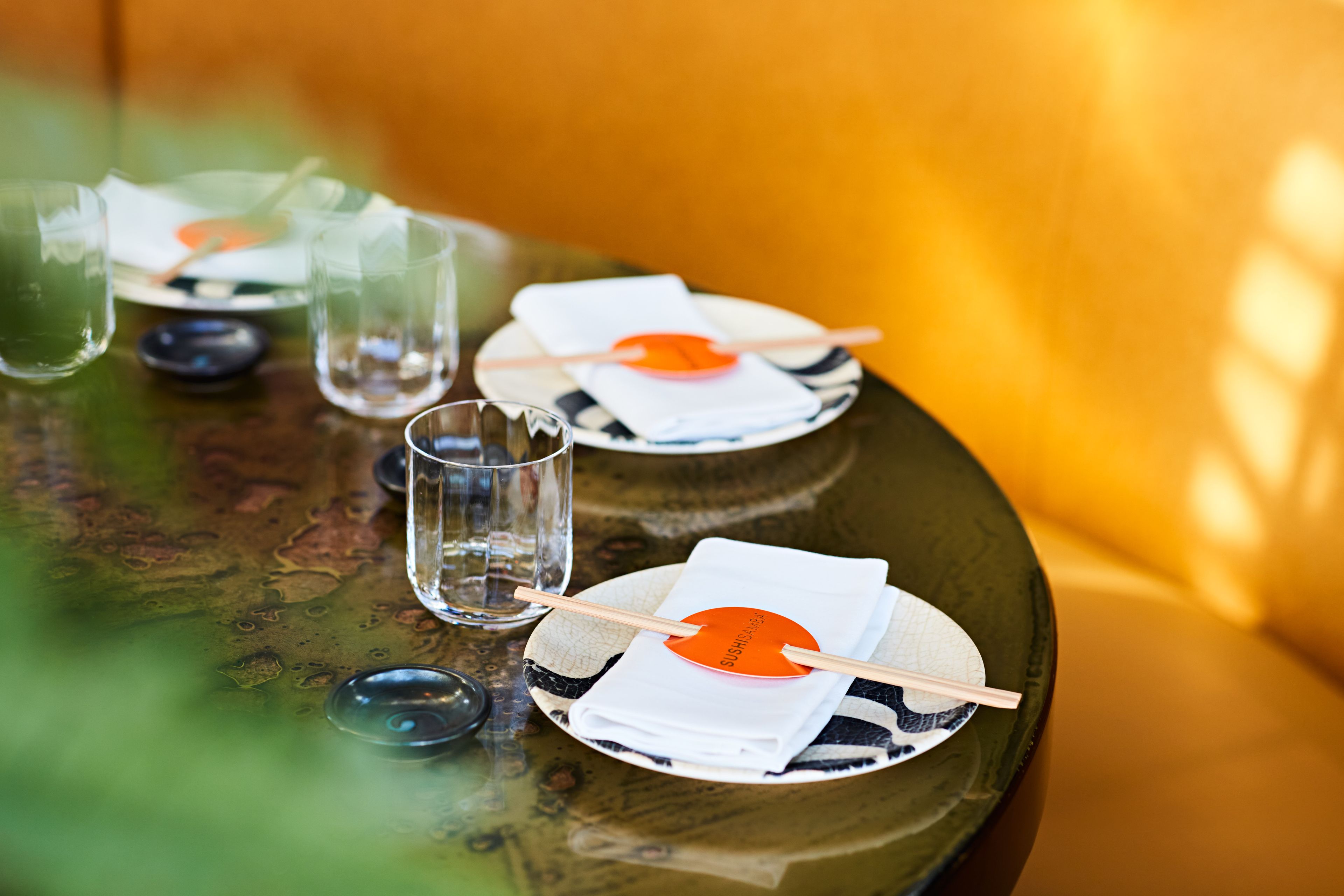 SUSHISAMBA Japanese Brazilian and Peruvian menus, a table set for dinner with plates, chopsticks and napkins in a yellow booth.